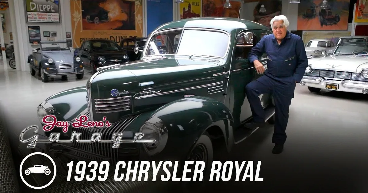 A man stands beside a classic dark green 1940s Chevrolet in a showroom filled with vintage cars.