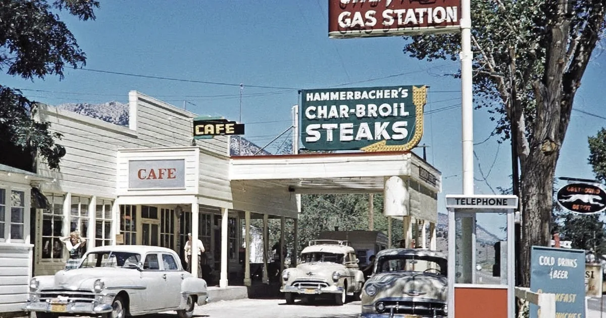 Vintage cars and people in a scenic, mountainous area with a clear sky.