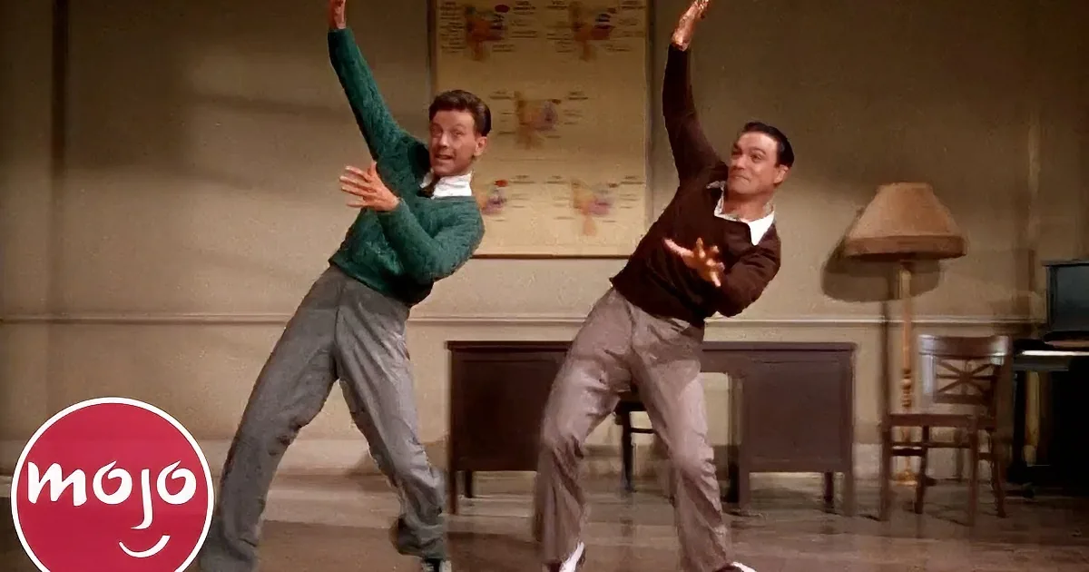 Two men in mid-dance, one in green sweater, the other in brown, performing a synchronized routine on stage.