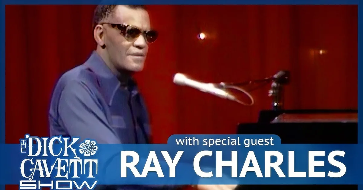 A man in a suit and sunglasses sings into a microphone on stage.
