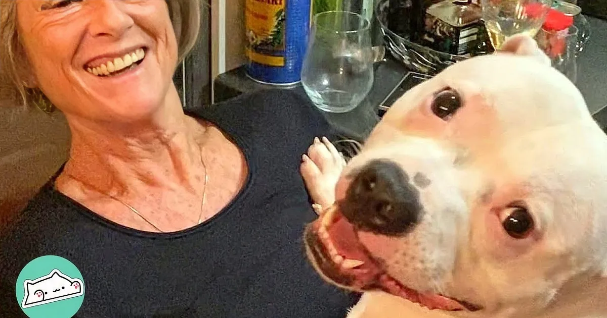A woman holds a white dog with a black nose, both looking at each other affectionately.
