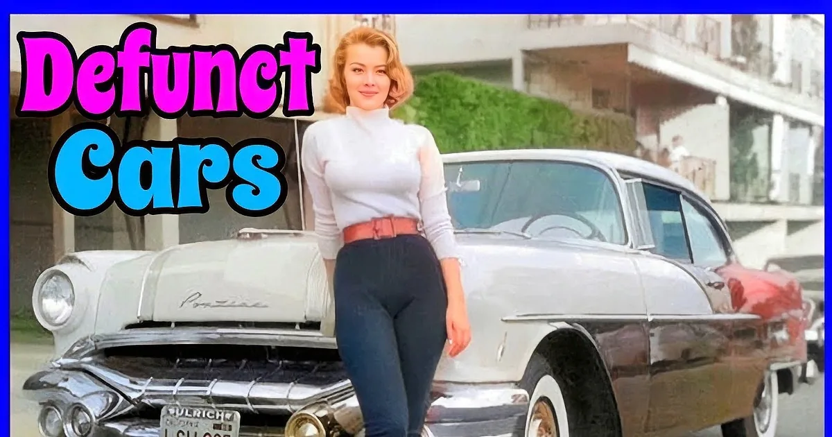 A woman in white pants sits on a cream-colored vintage car by a lake.