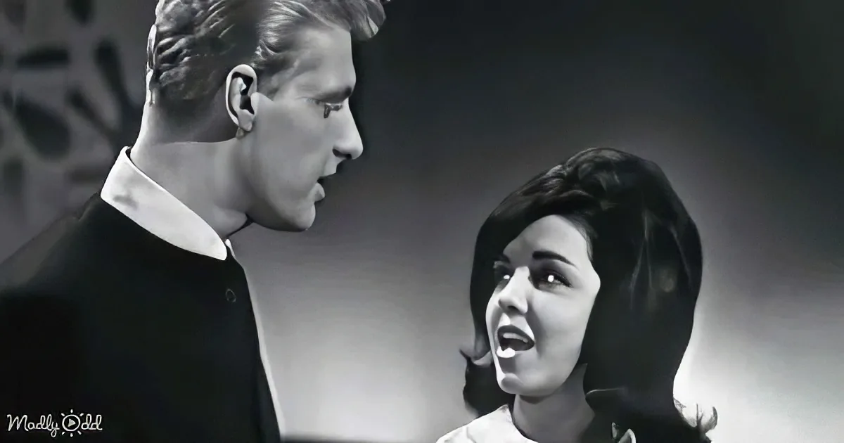 A man and woman are facing each other, the woman appears to be speaking or singing with her mouth open.