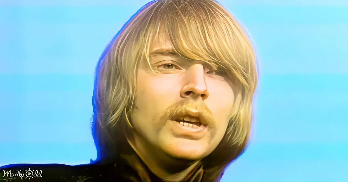 A person with long, light brown hair and a mustache is shown against a blue background.
