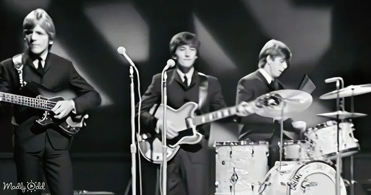 The Beatles perform on stage, dressed in suits, with microphones and instruments, under dramatic lighting.