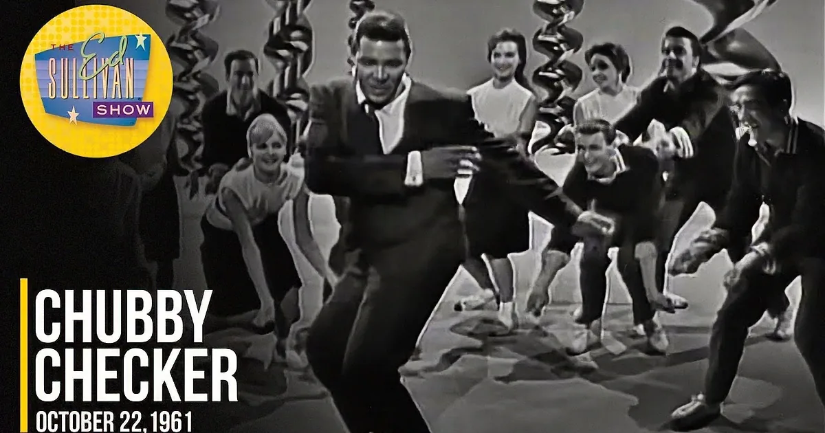 A man in a suit dances joyfully with a group of people in a lively, celebratory scene.
