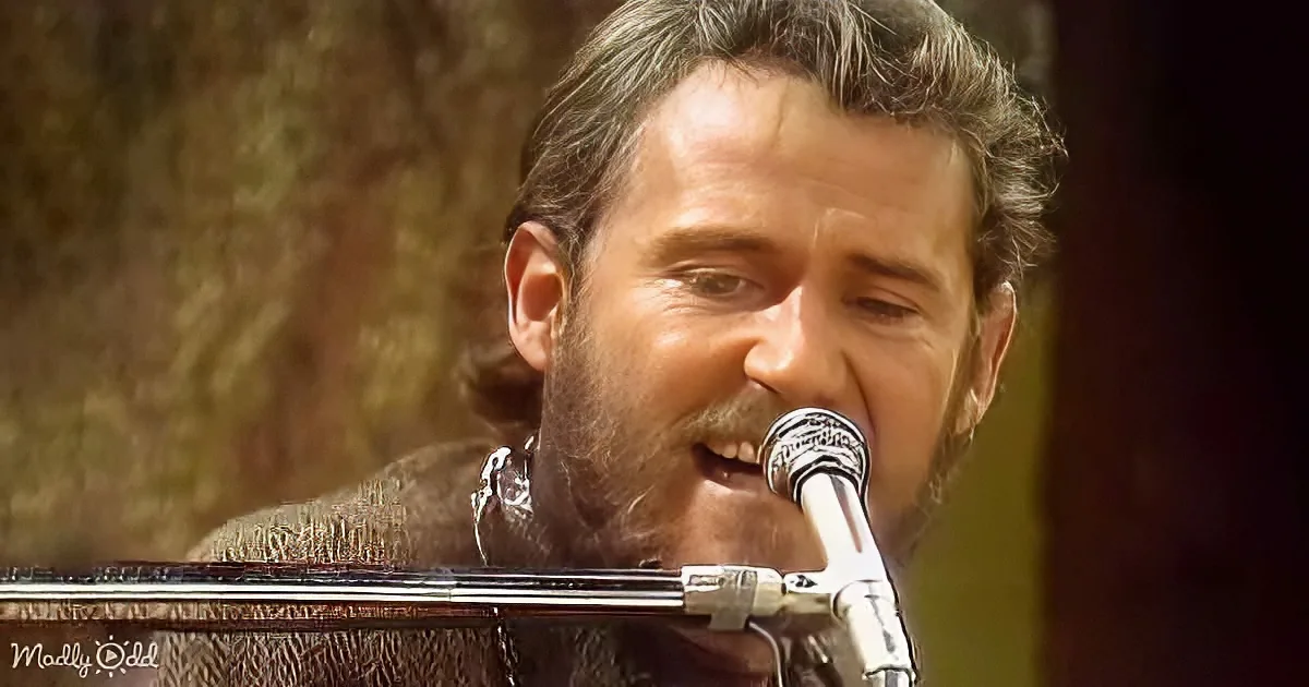 A man with a beard sings into a microphone, wearing a textured brown jacket.