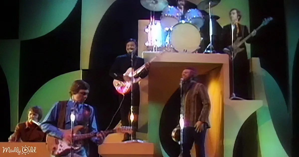 A band performs on stage with a colorful backdrop, featuring a guitarist, drummer, and singer.