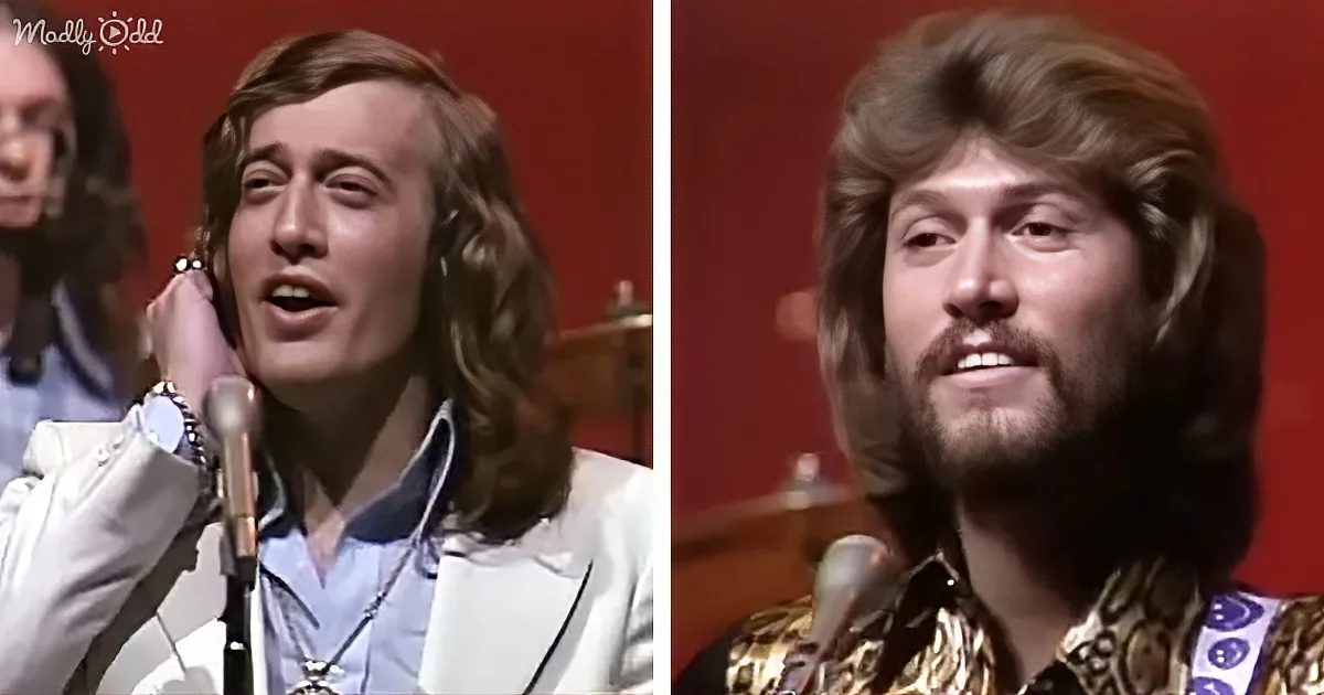 A man with long hair and a beard sings into a microphone, wearing a white jacket and a gold shirt.