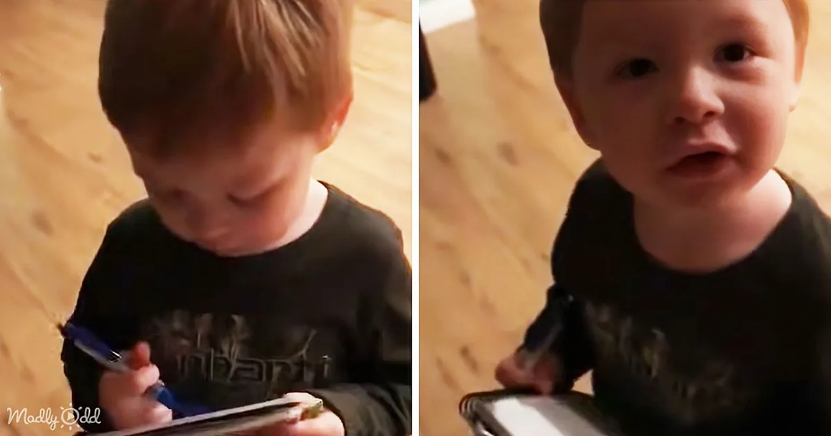 A young child in a black shirt is holding a pen and appears to be looking at something in their hands.