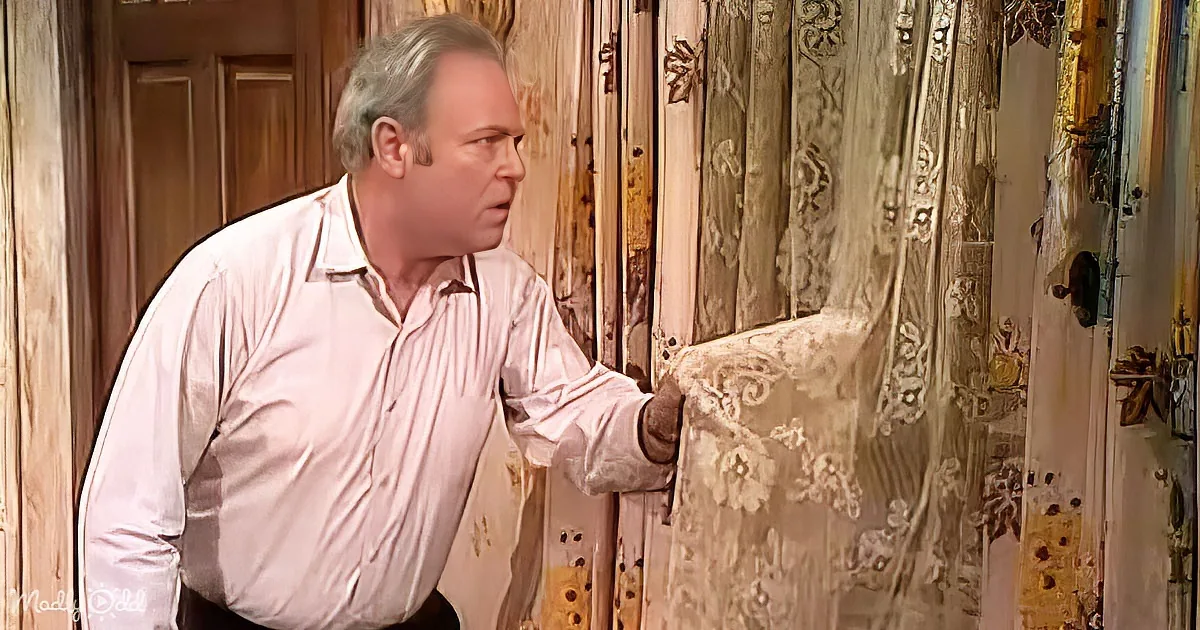 A man in a white shirt leans against a wooden door, looking concerned.