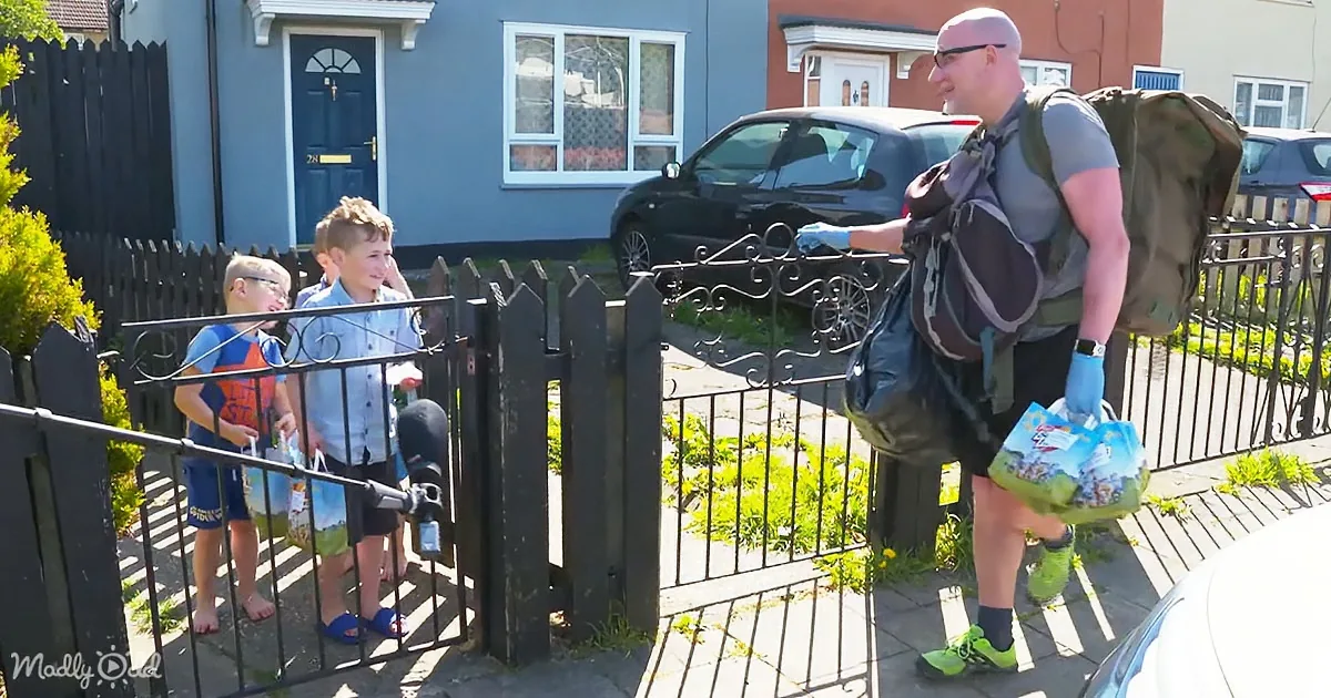 A man with a backpack and gloves carries bags, interacting with two children at a gate.