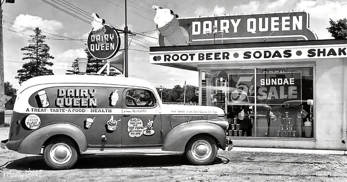 A vintage Dairy Queen delivery van parked in front of a Dairy Queen store with a sign advertising root beer, sodas...
