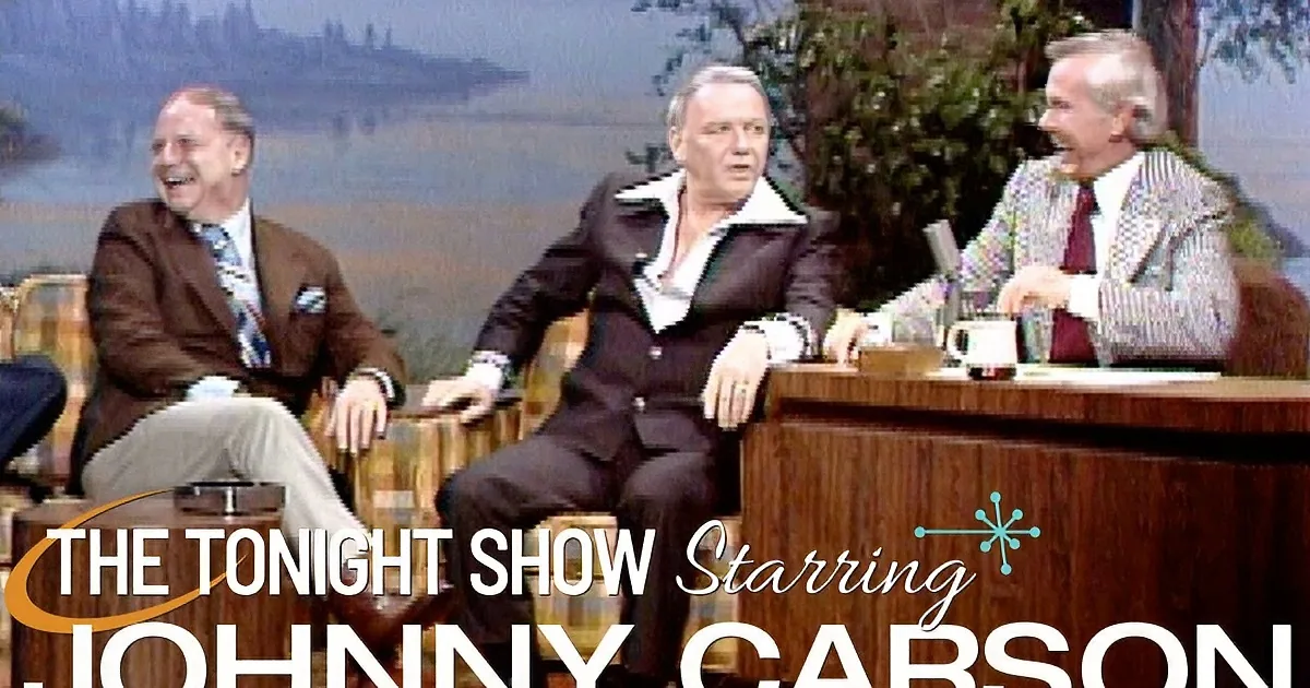 Frank Sinatra sits on a couch, laughing, with two other men and a host on a talk show set.