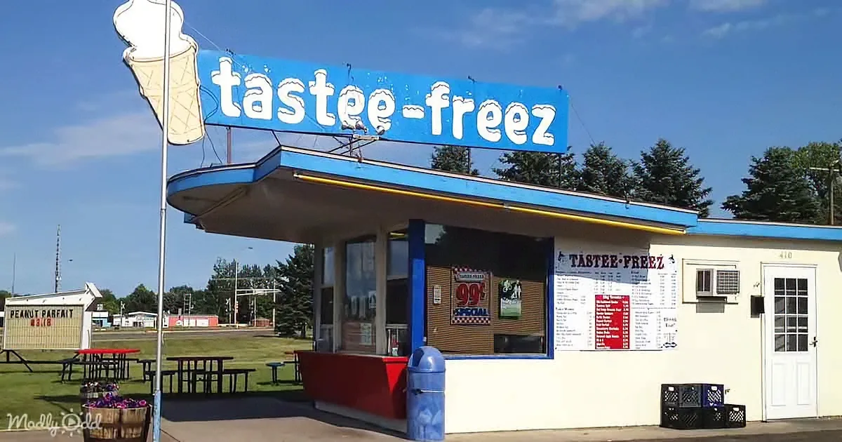 A Tastee-Freez ice cream stand with a blue sign, red counter, and picnic tables under a clear sky.