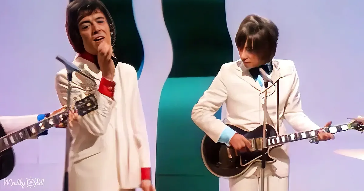 A man in a white suit plays a guitar on stage, singing into a microphone.