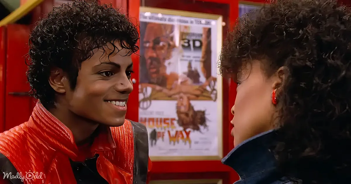 A person in a red jacket smiles at another person with curly hair, in front of a "House of Wax" poster.