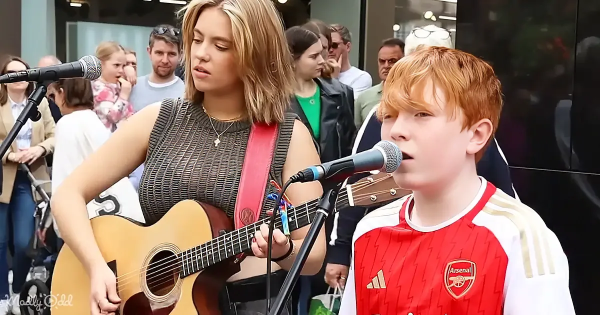 A woman plays guitar while a boy sings into a microphone in front of a crowd.