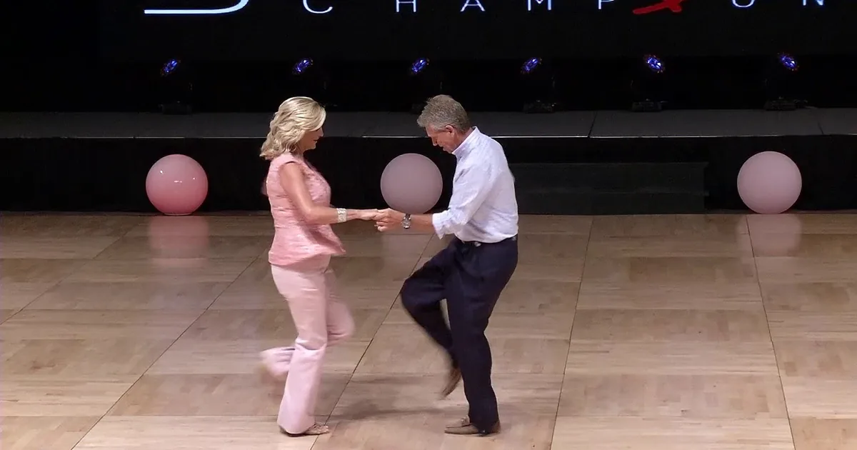 A man and woman are dancing together on a wooden floor, holding hands, with balloons in the background.