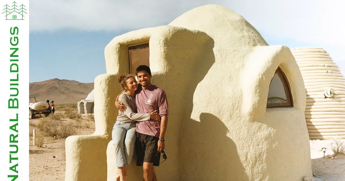 A couple hugs in front of a unique, sand-colored, dome-shaped structure in a desert landscape.