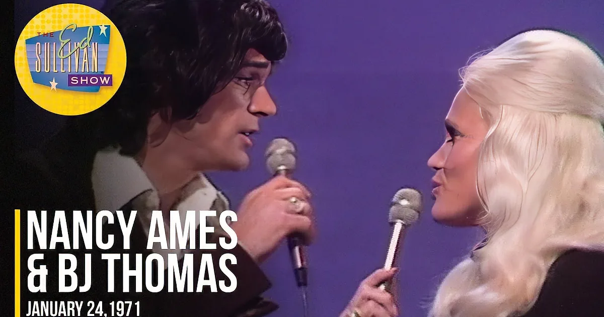 A man with dark hair and a woman with blonde hair are singing into microphones on stage.