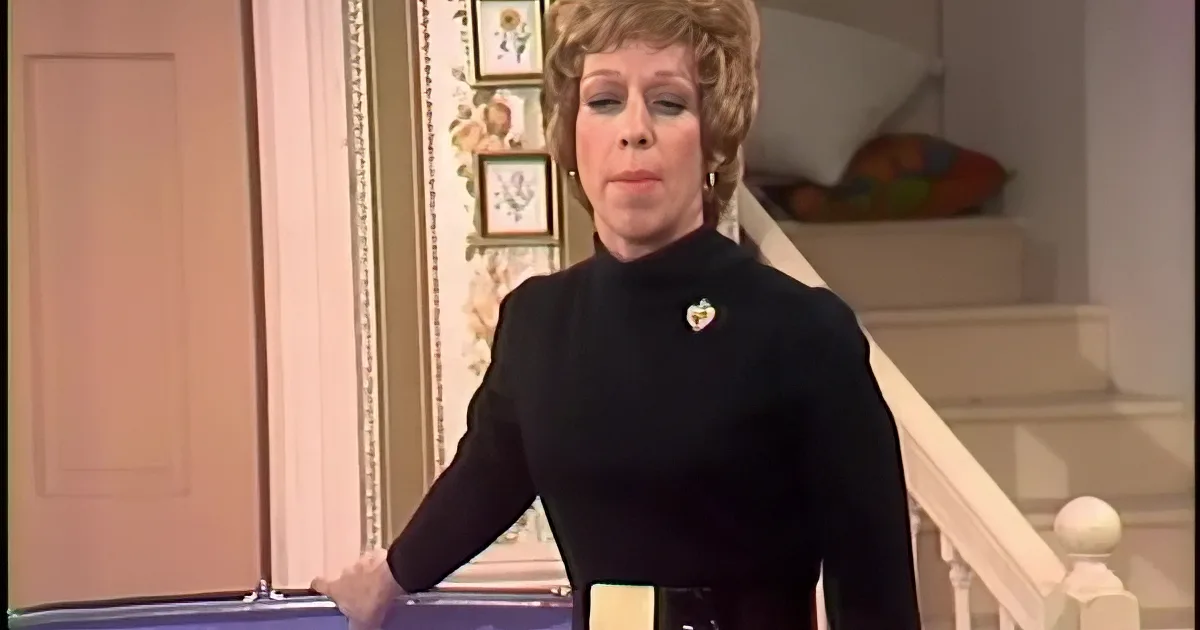Woman in black holds yellow paper, looks at man in beige shirt, both in room with artwork.
