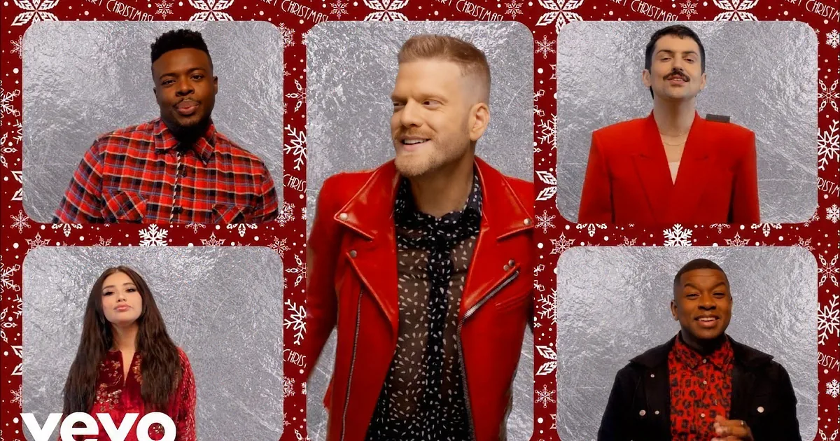 Two individuals in shiny silver jackets stand against a red background, surrounded by other people in festive attire.