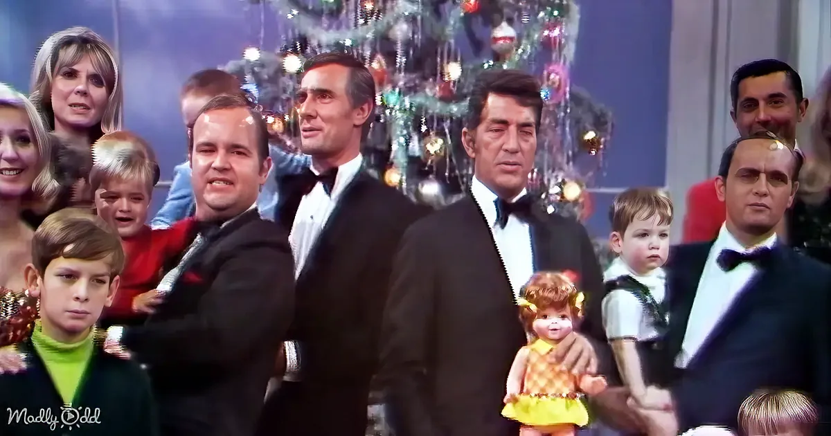 A group of people in formal attire stands in front of a decorated Christmas tree, with a child holding a doll.