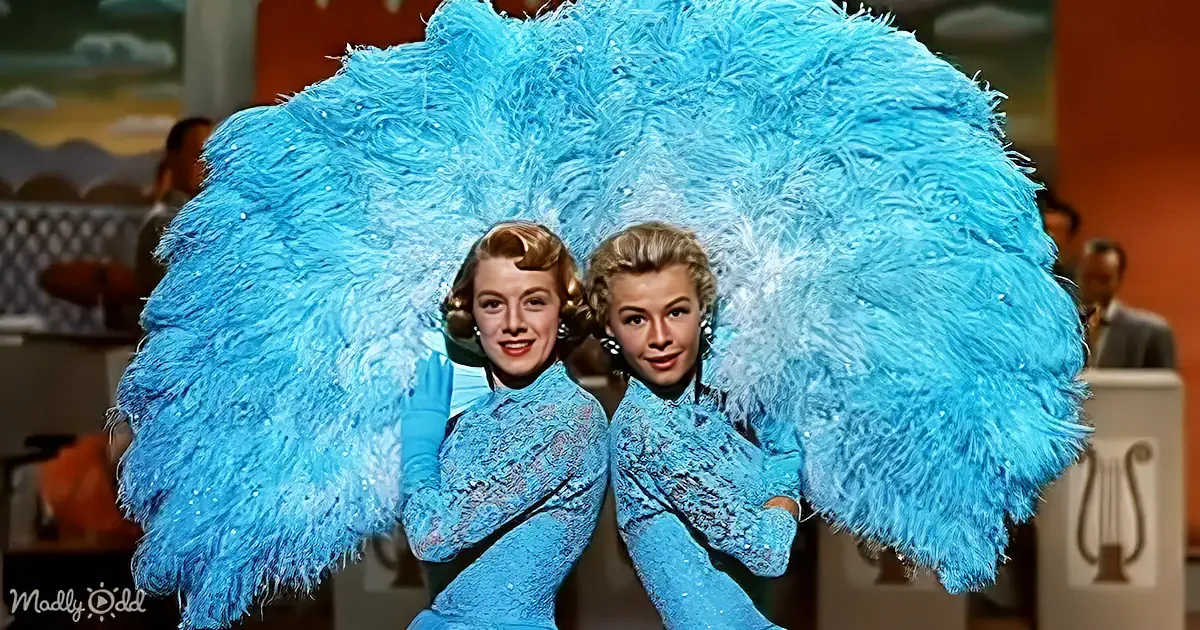 Two women in matching blue costumes with large feathered wings pose together.