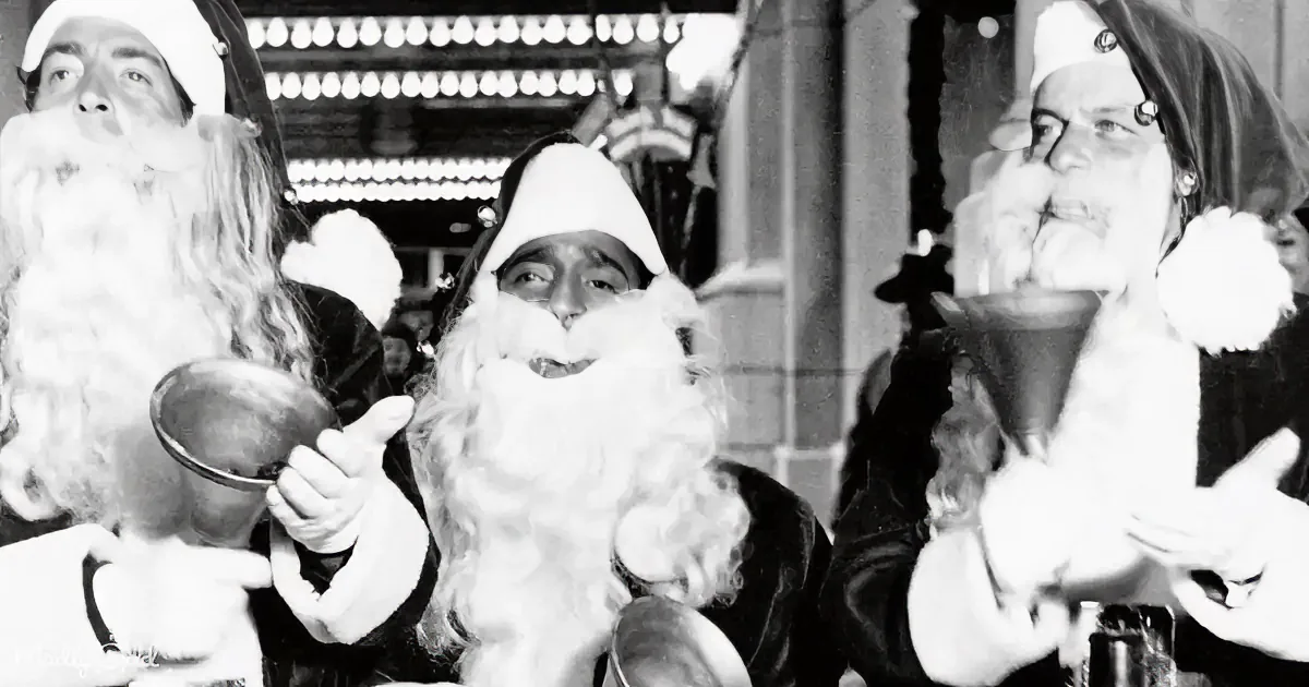 A man dressed as Santa Claus holds a bell, surrounded by other Santas in a festive setting.