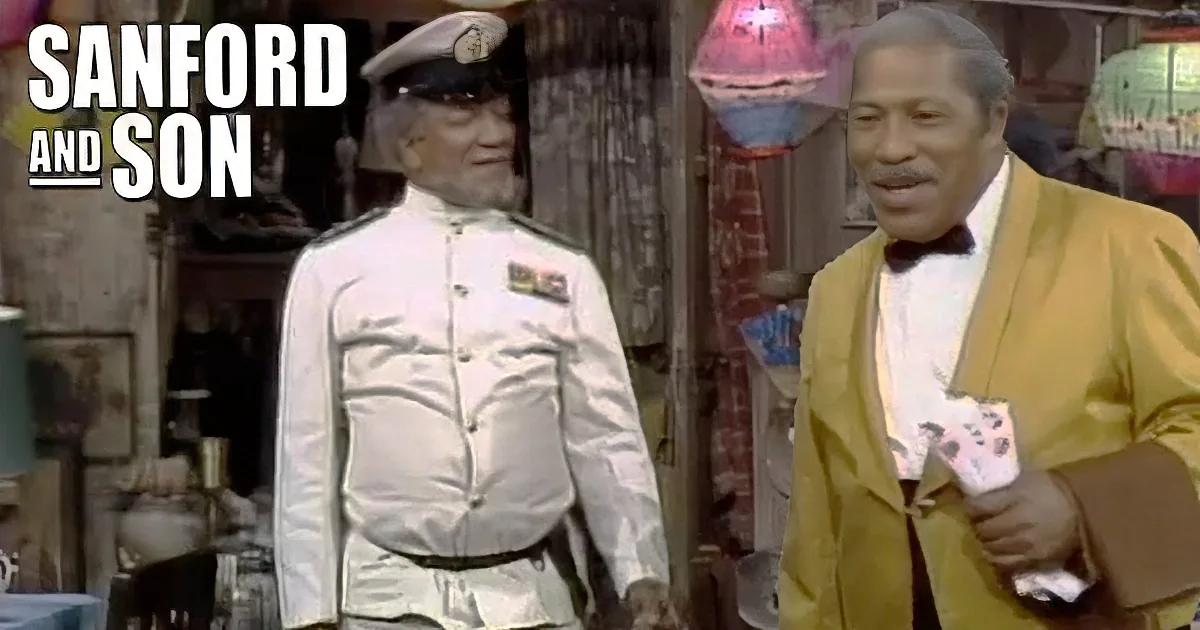 A man in a white uniform and cap stands next to another man in a yellow suit, both smiling.