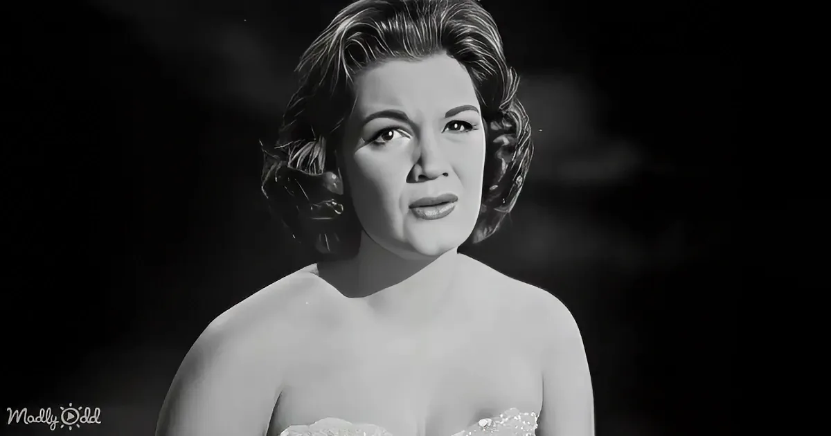A woman with short, styled hair, wearing a strapless dress, gazes upward in a black-and-white portrait.