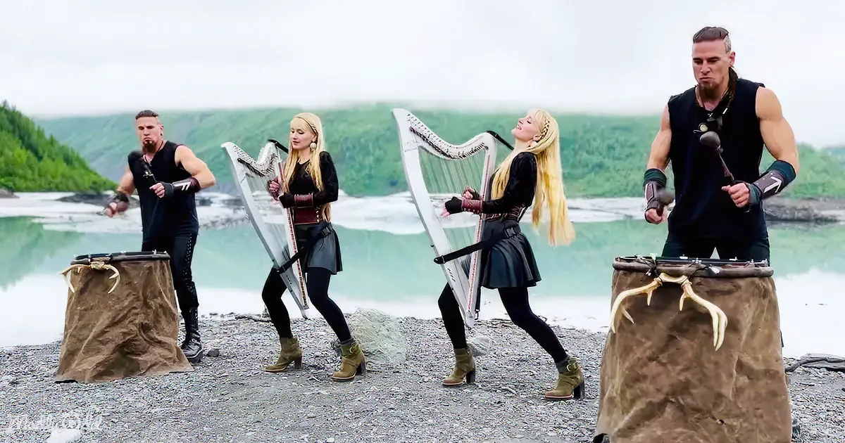 Four musicians in Viking attire play harps and drums by a serene lake.