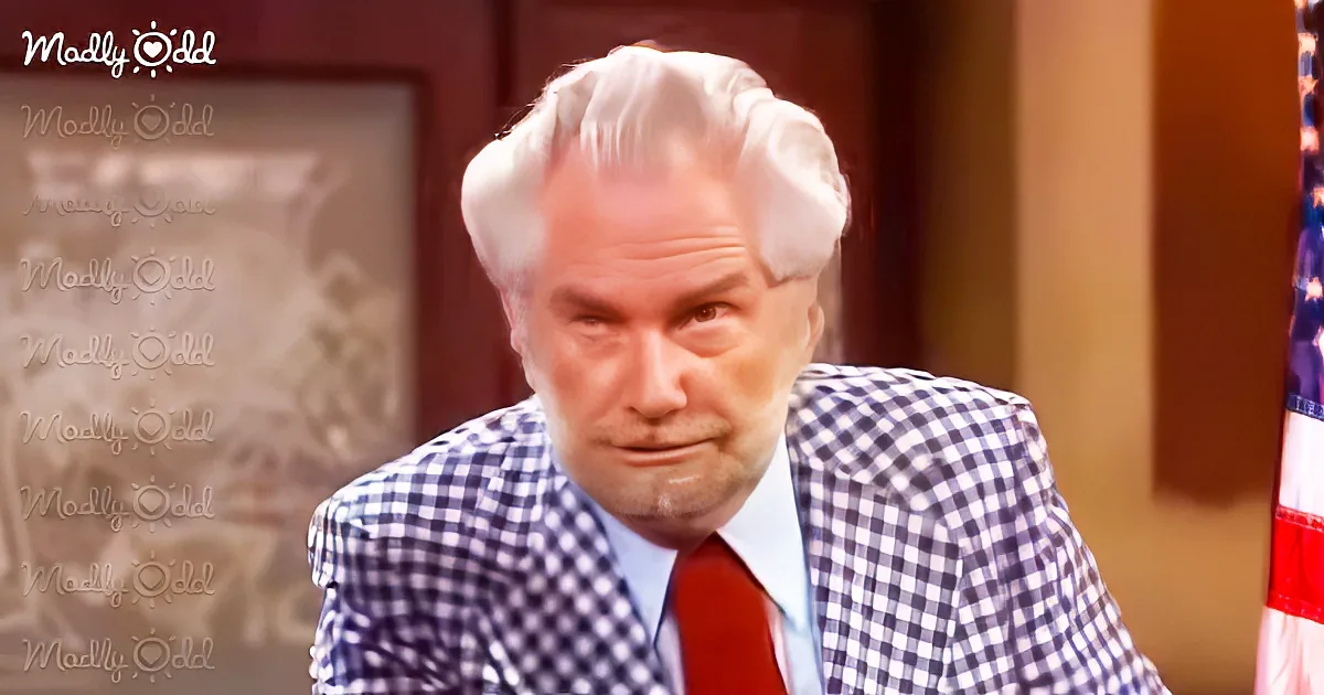 A man in a checkered suit and red tie looks distressed, with a blurred background and "Madly Odd" watermark.