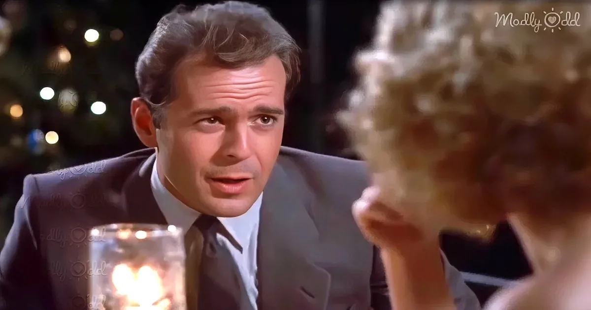 A man in a suit leans forward, looking intently at a woman with curly hair, in a warmly lit setting.