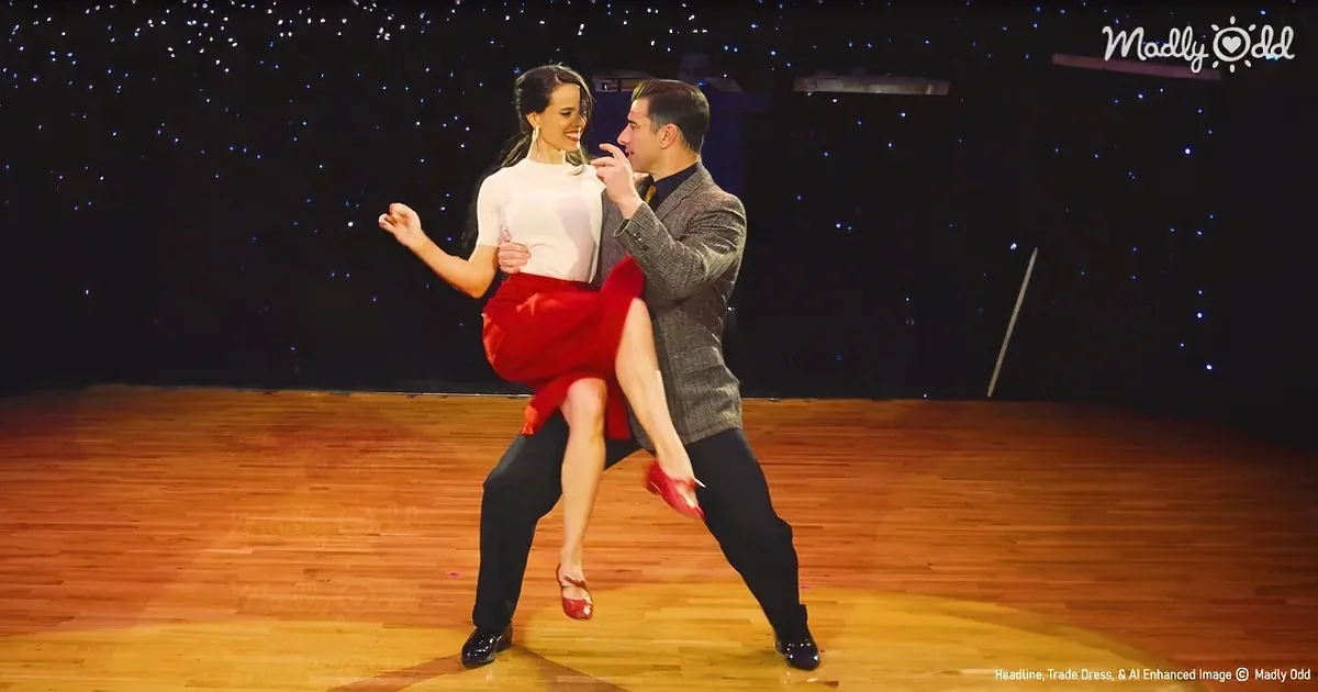 A couple dances elegantly on a wooden floor, the woman in a red skirt and white top, the man in a dark suit.