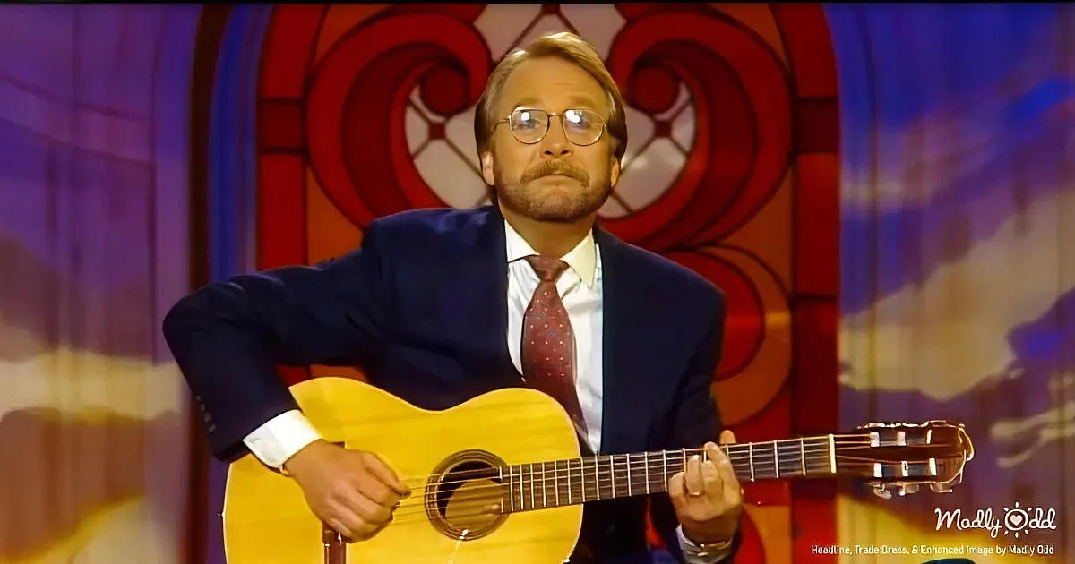 A man in a suit plays a yellow guitar on a stage with a colorful background.