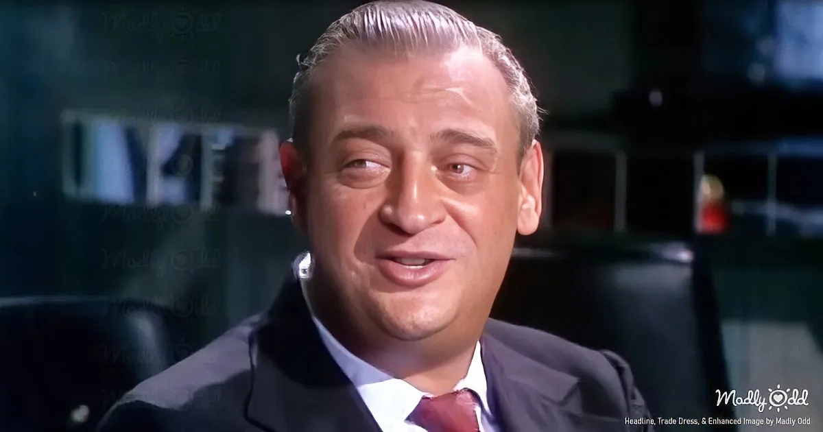 A man in a suit and tie, with slicked-back hair, is seated in a dimly lit room, looking slightly to the side.