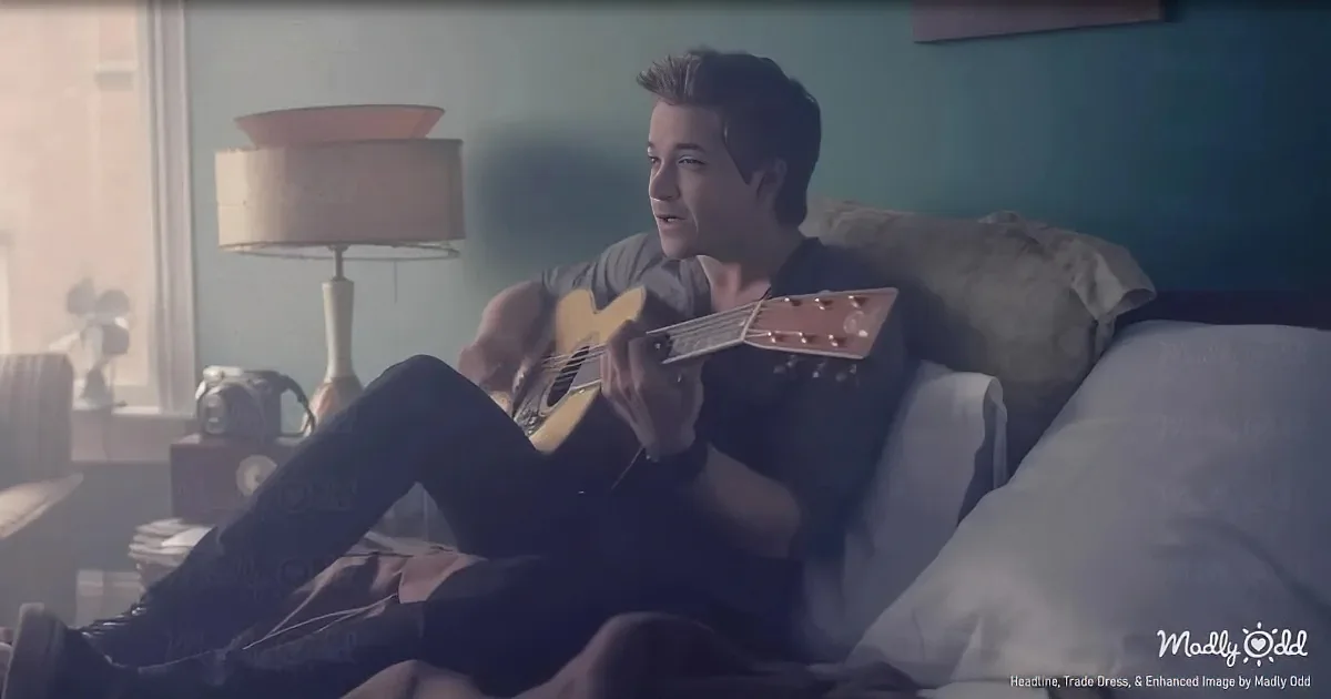 A person sits on a bed playing a guitar, surrounded by a cozy room with a lamp and window.