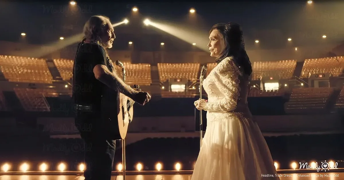 A man and woman stand on stage, the man holding a guitar, both smiling at each other.