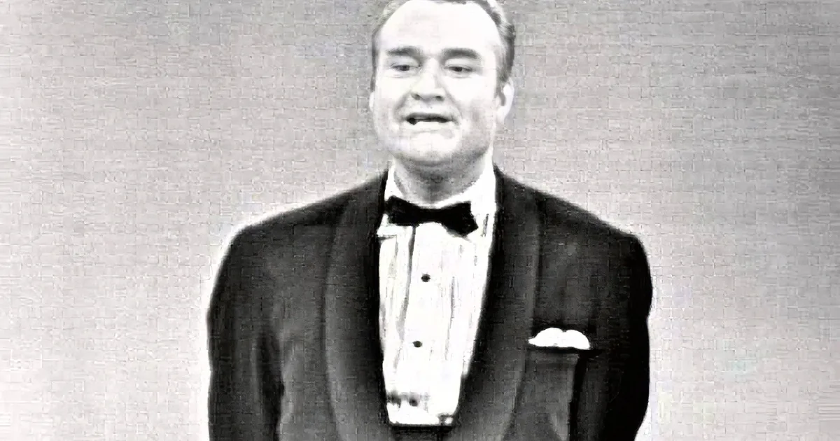 A man in a tuxedo with a bow tie and pocket square, looking surprised or shocked.