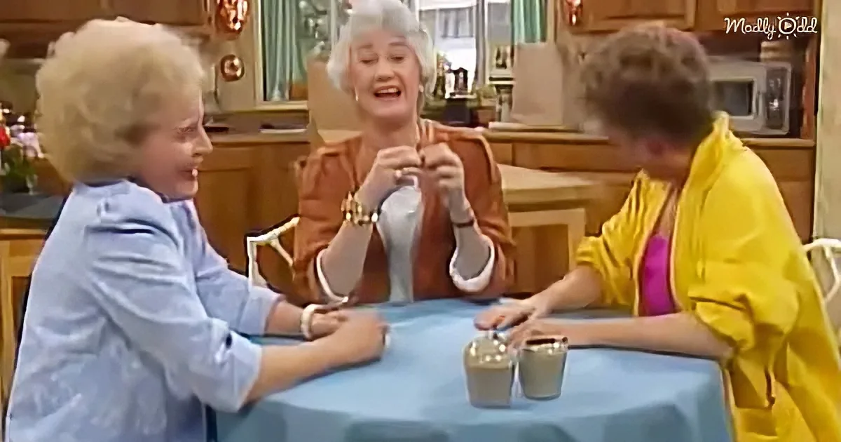 Three women sit at a table, one knitting, another laughing, and the third leaning forward, in a cozy kitchen setting.