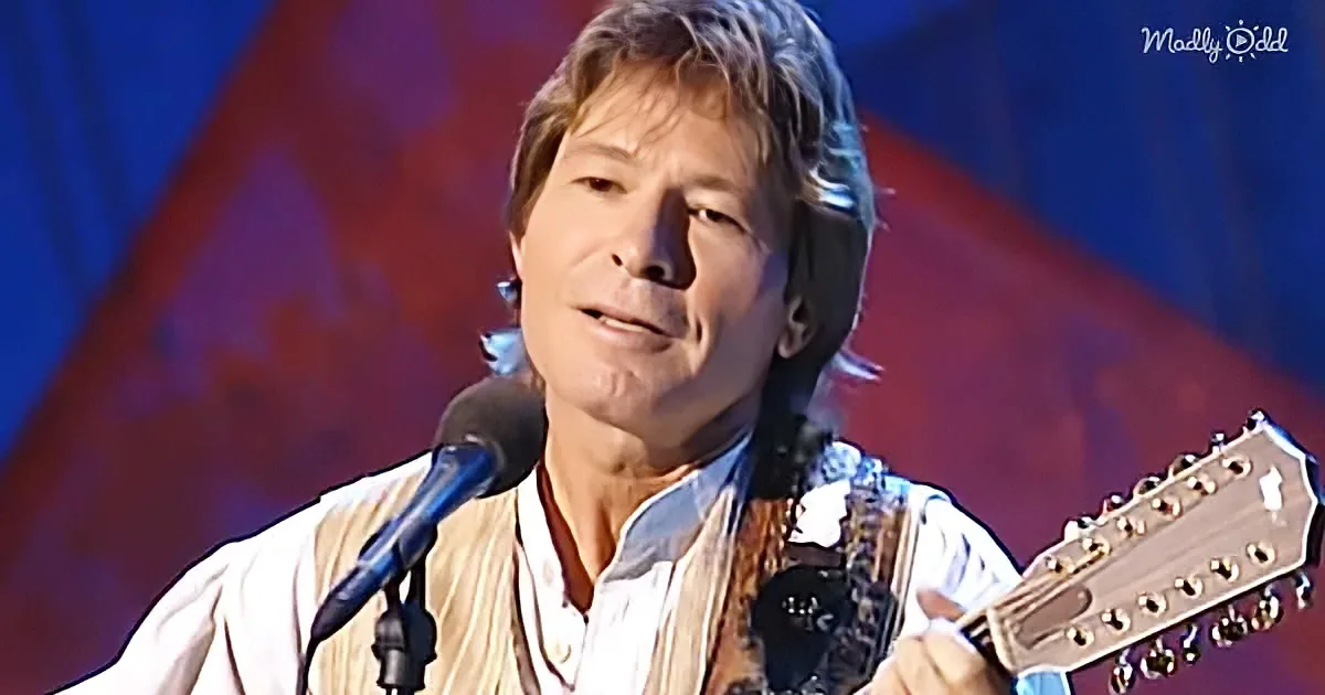 A man with shoulder-length hair plays a guitar while singing into a microphone.