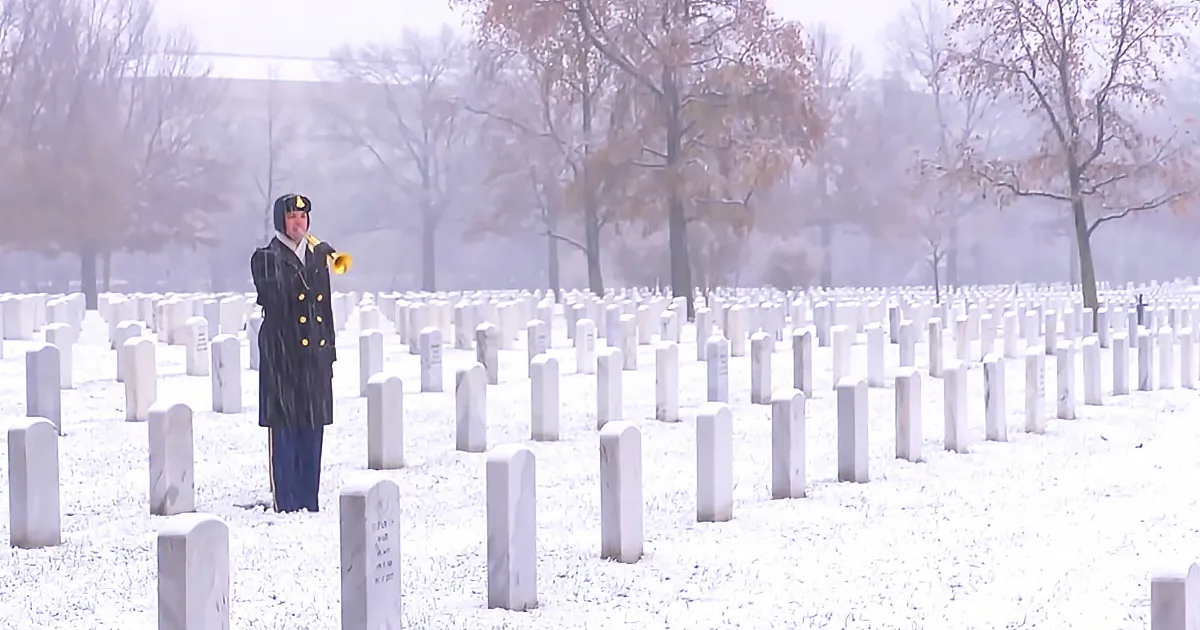 A person in a military uniform stands amidst snow-covered headstones in a cemetery.