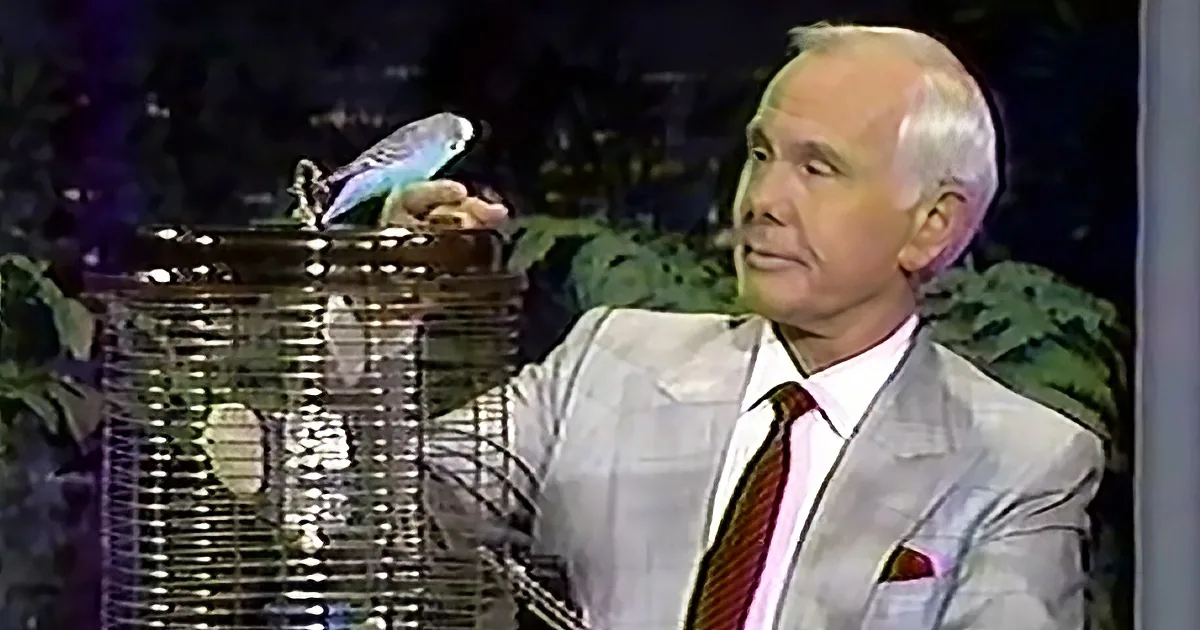 A man in a suit holds a birdcage with a blue bird perched on top.