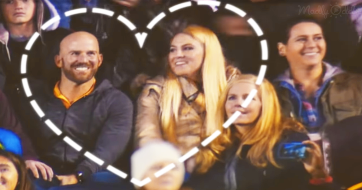 A man with a bald head and a smile is surrounded by a group of people in a crowd setting.